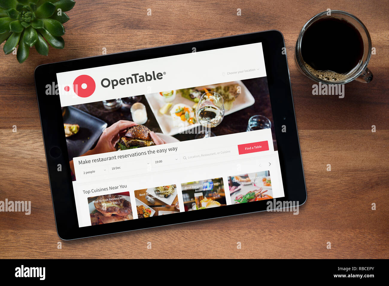 Il sito web di OpenTable è visto su un tablet iPad, su di un tavolo di legno lungo con un caffè espresso e una pianta di casa (solo uso editoriale). Foto Stock