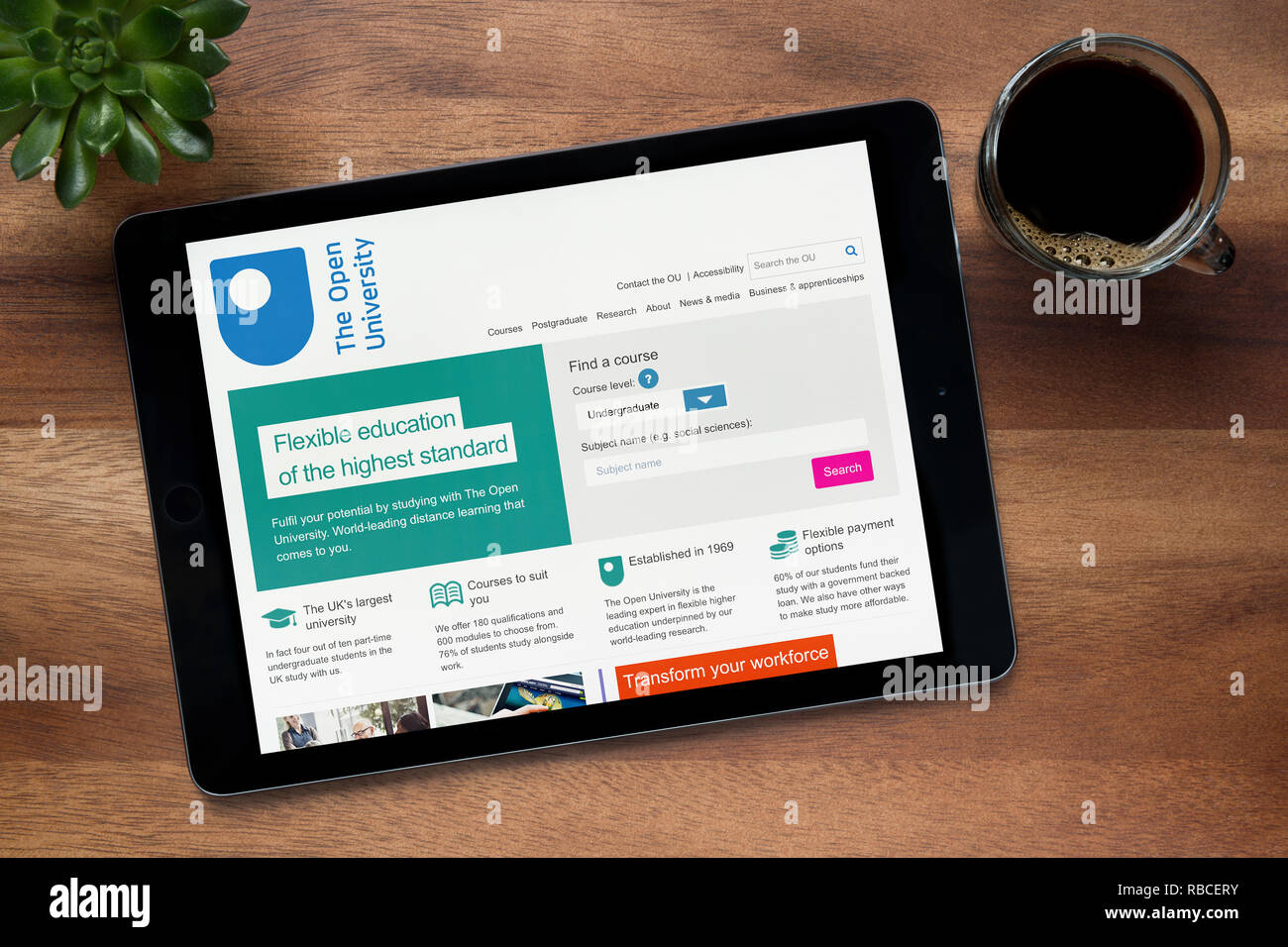 Il sito web dell'università aperta è visto su un tablet iPad, su di un tavolo di legno lungo con un caffè espresso e una pianta di casa (solo uso editoriale). Foto Stock