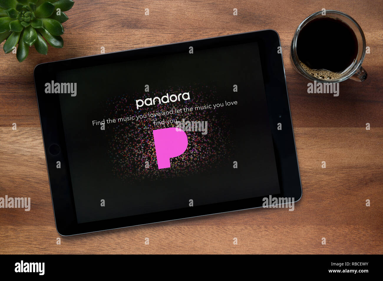 Il sito web di Pandora è visto su un tablet iPad, su di un tavolo di legno lungo con un caffè espresso e una pianta di casa (solo uso editoriale). Foto Stock