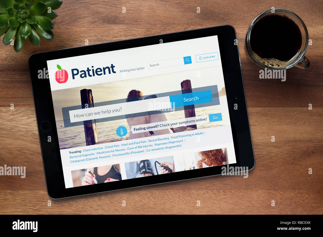 Il sito web del paziente è visto su un tablet iPad, su di un tavolo di legno lungo con un caffè espresso e una pianta di casa (solo uso editoriale). Foto Stock