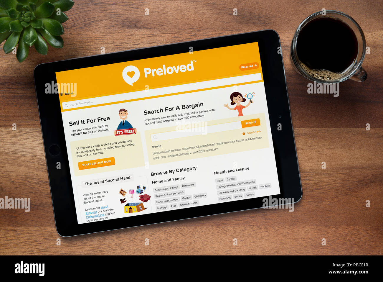 Il sito web di Preloved è visto su un tablet iPad, su di un tavolo di legno lungo con un caffè espresso e una pianta di casa (solo uso editoriale). Foto Stock