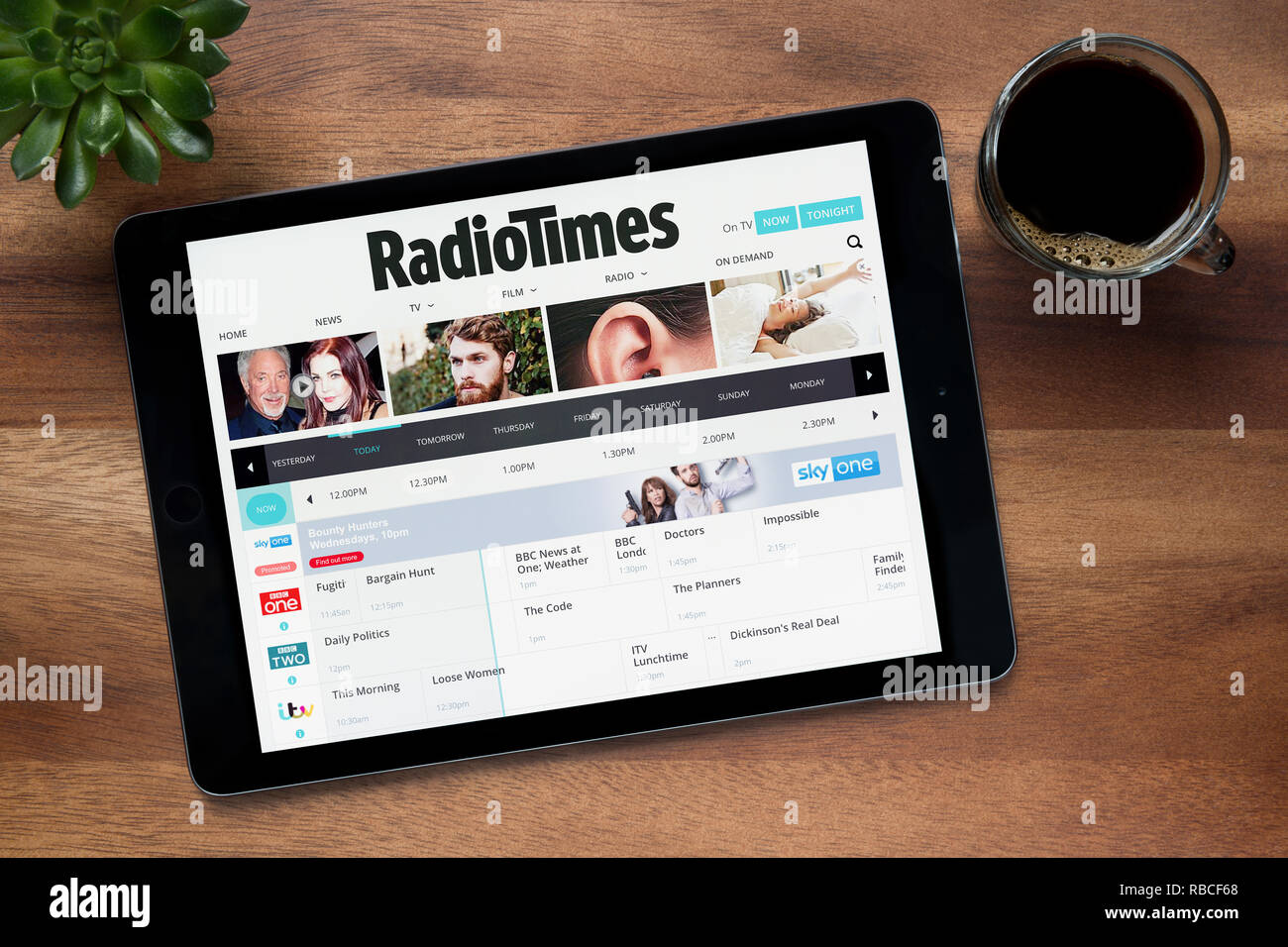 Il sito di Radio Times è visto su un tablet iPad, su di un tavolo di legno lungo con un caffè espresso e una pianta di casa (solo uso editoriale). Foto Stock