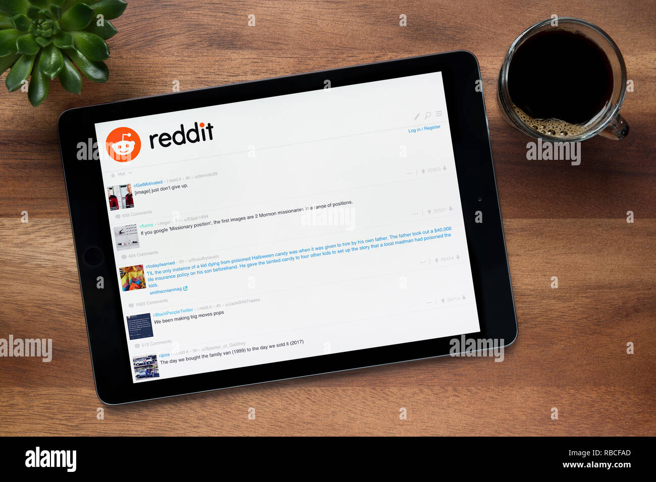 Il sito web di Reddit è visto su un tablet iPad, su di un tavolo di legno lungo con un caffè espresso e una pianta di casa (solo uso editoriale). Foto Stock
