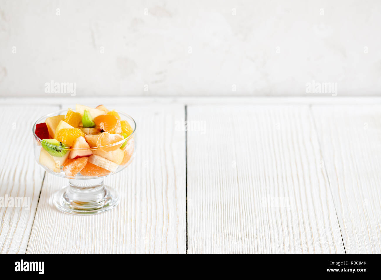 Vaso di vetro con insalata di frutta è in piedi sul bianco tavola di legno. Foto Stock