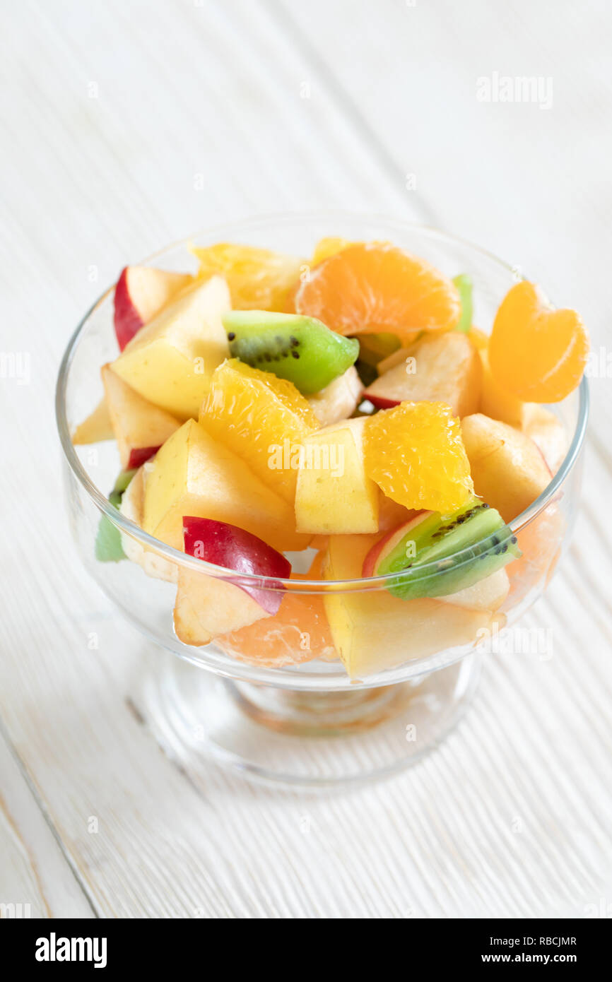 Close-up ciotola di vetro con insalata di frutta su bianco tavolo in legno. Foto Stock