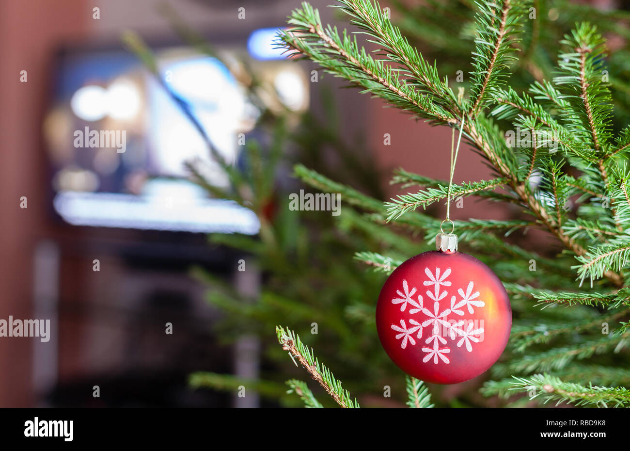Palla di vetro sul verde ramoscelli di vivere albero di Natale e la TV sullo sfondo a casa indoor Foto Stock