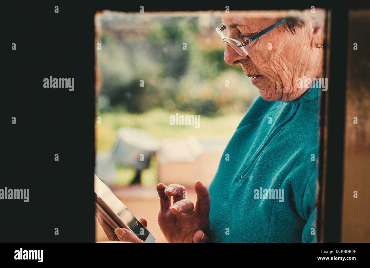 Colpo di un vecchio attraente donna in piedi dietro una finestra di vetro mentre utilizzando il suo telefono mobile e messaggistica di testo Foto Stock