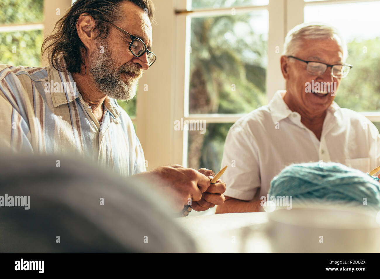 Barba Senior uomo maglia con un amico seduto da e sorridente in ambienti chiusi. Due pensionati uomini facendo passatempo a casa. Foto Stock