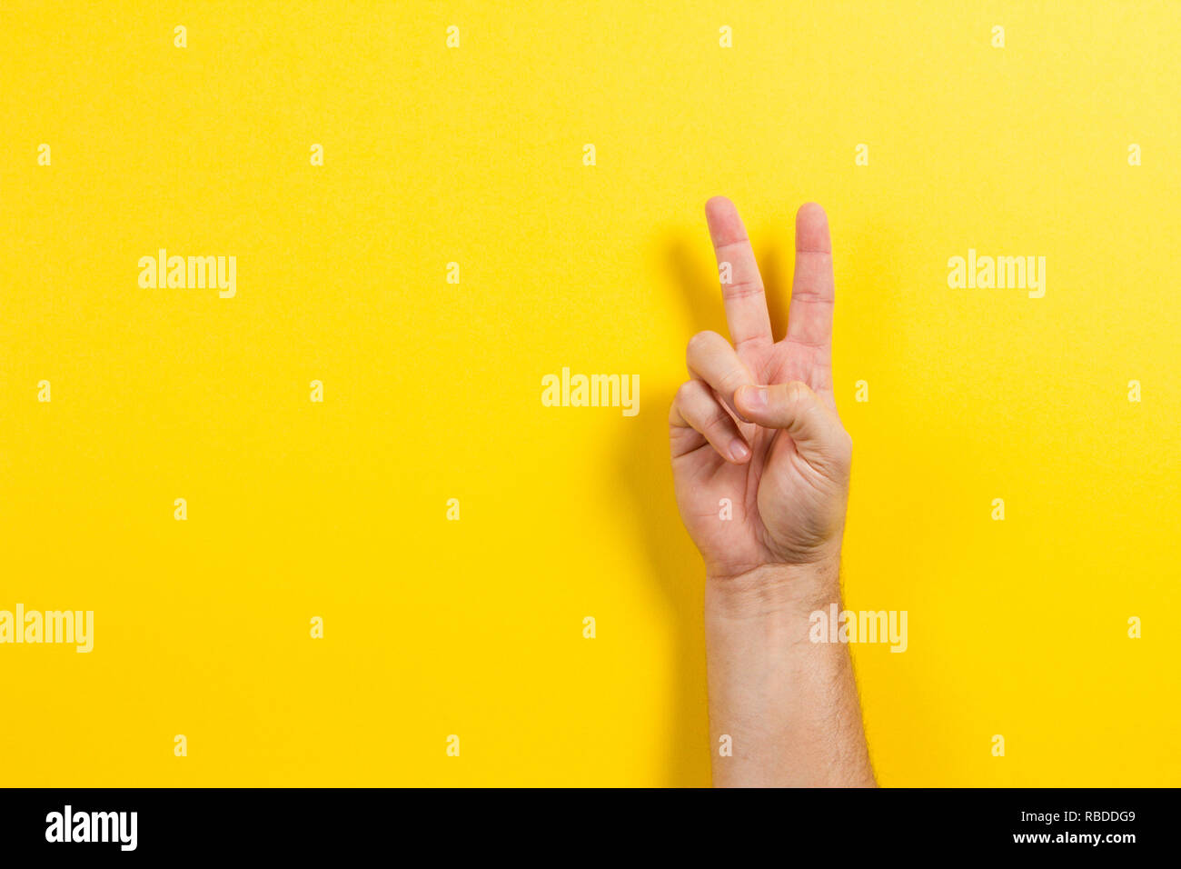 Man mano che mostra due dita su sfondo giallo. Il numero due simbolo Foto Stock