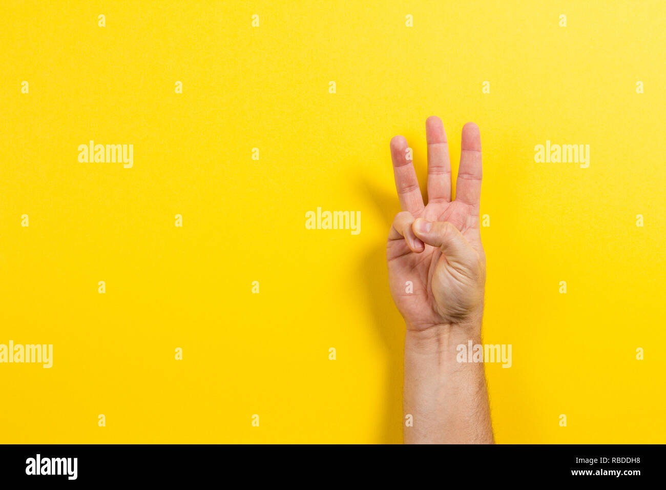 Man mano che mostra tre dita su sfondo giallo. Il numero due simbolo Foto Stock