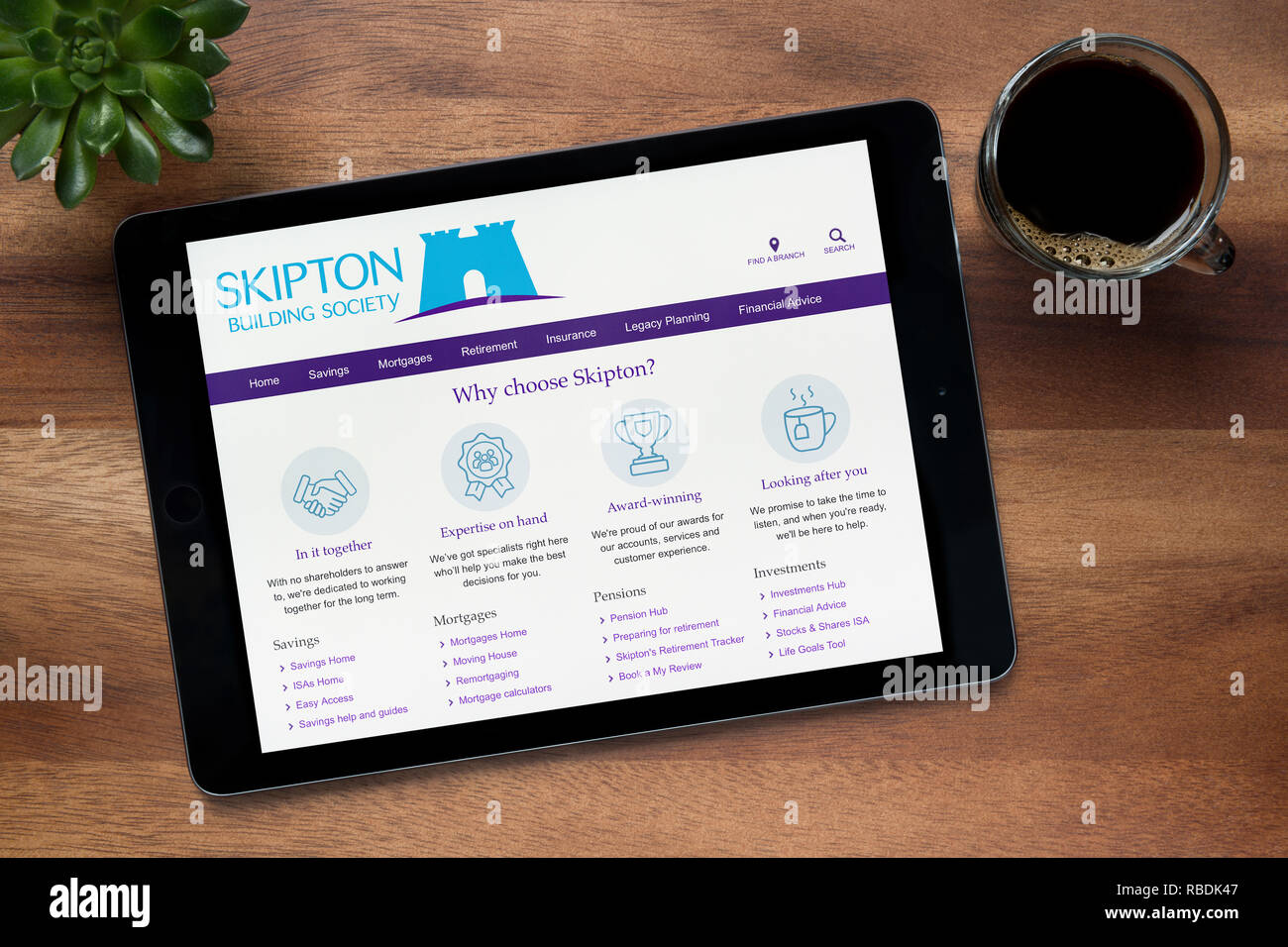 Il sito web di Skipton Building Society è visto su un tablet iPad, su di un tavolo di legno lungo con un caffè espresso e una pianta di casa (editoriale solo) Foto Stock