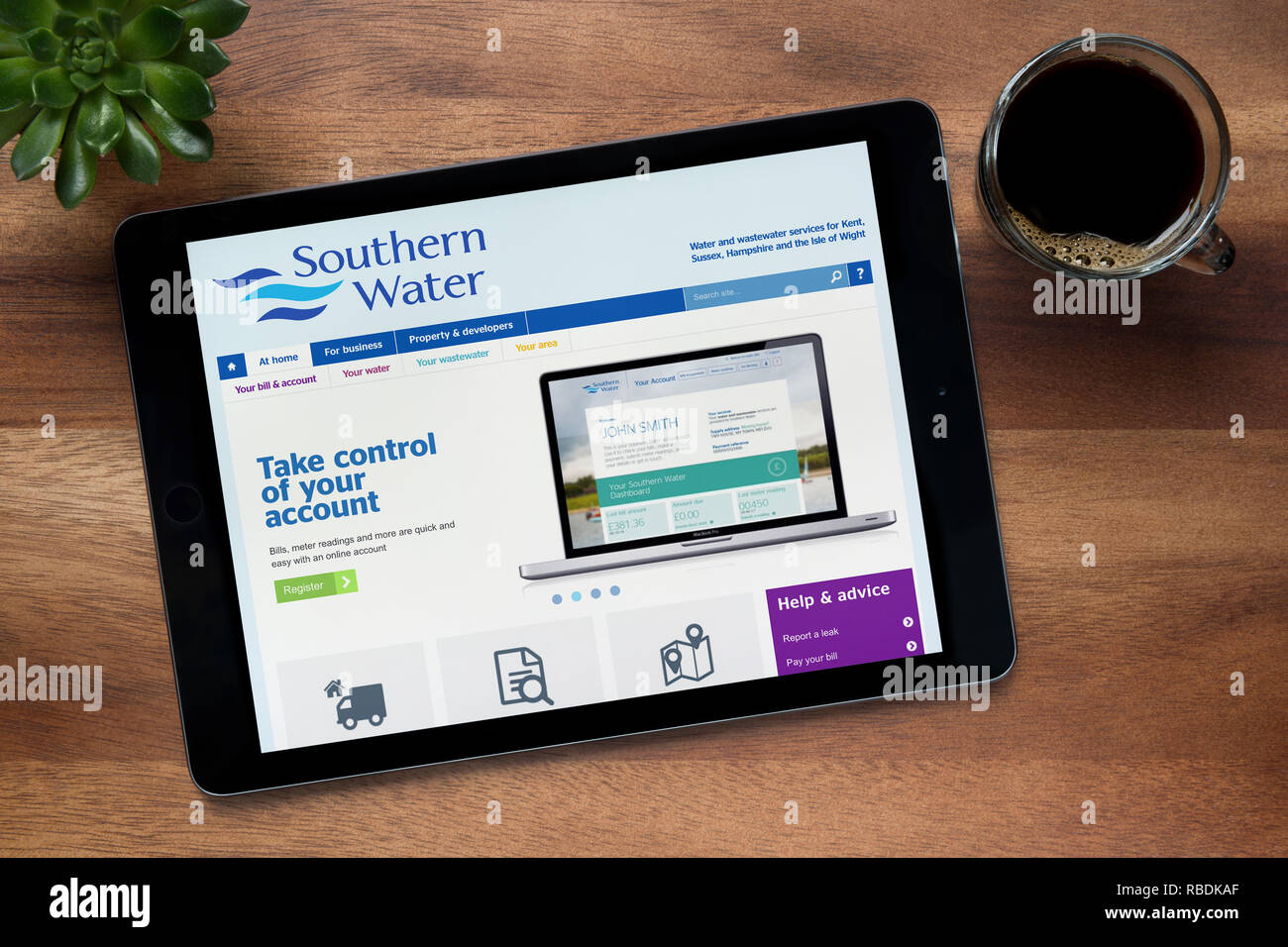 Il sito web del sud dell'acqua è visibile su un tablet iPad, su di un tavolo di legno lungo con un caffè espresso e una pianta di casa (solo uso editoriale). Foto Stock
