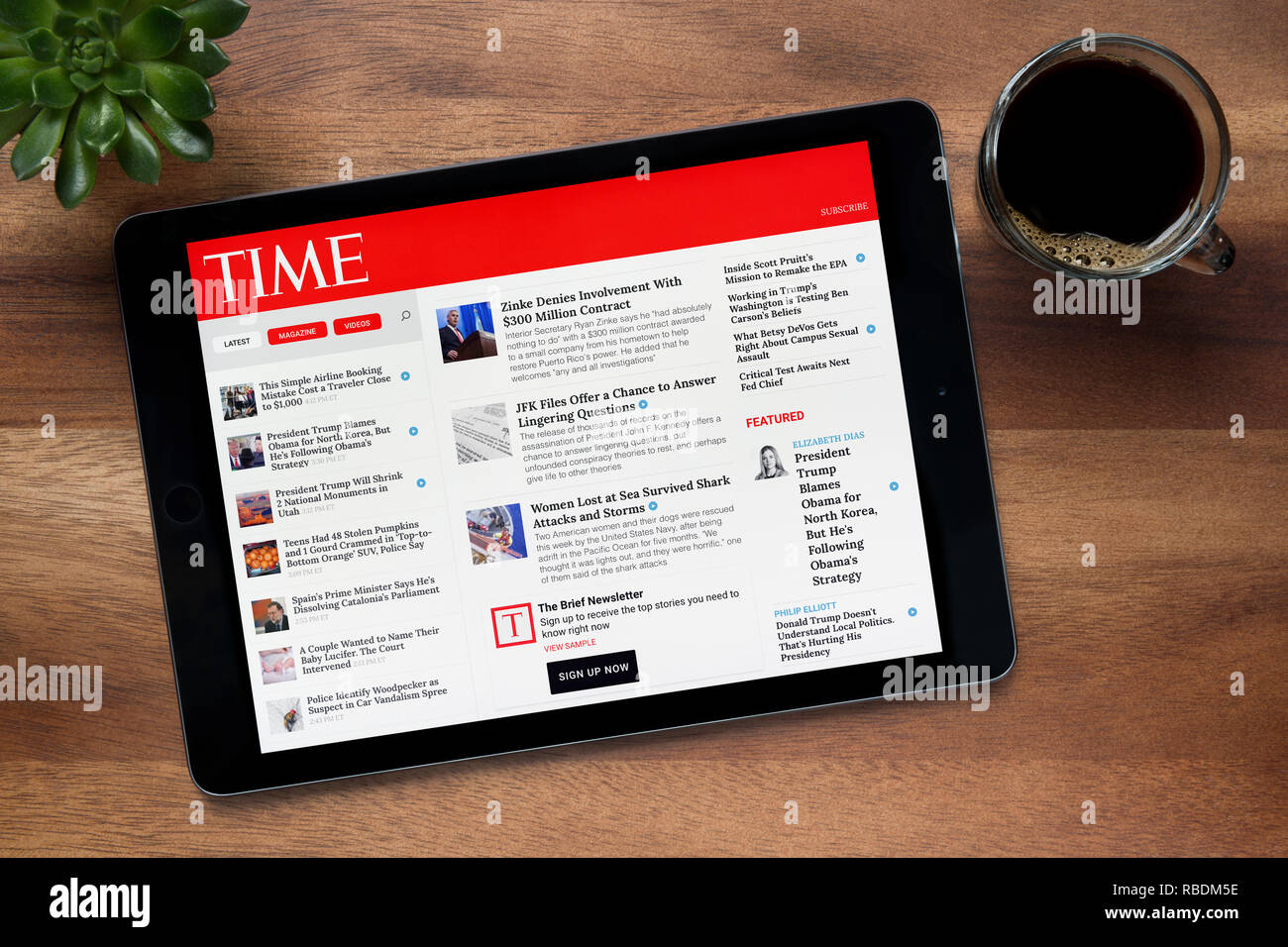 Il sito web della rivista Time è visto su un tablet iPad, su di un tavolo di legno lungo con un caffè espresso e una pianta di casa (solo uso editoriale). Foto Stock