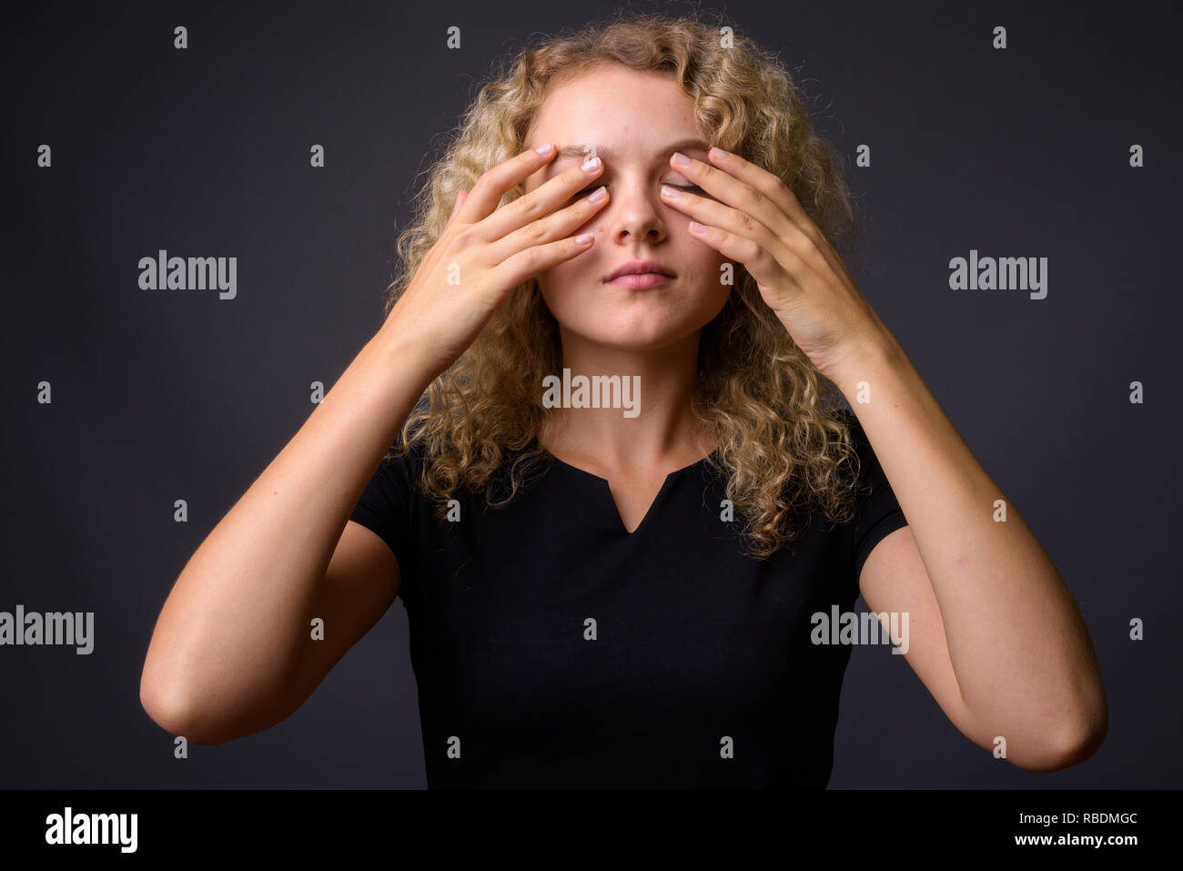 Giovane bella donna con ricci capelli biondi occhi di copertura Foto Stock