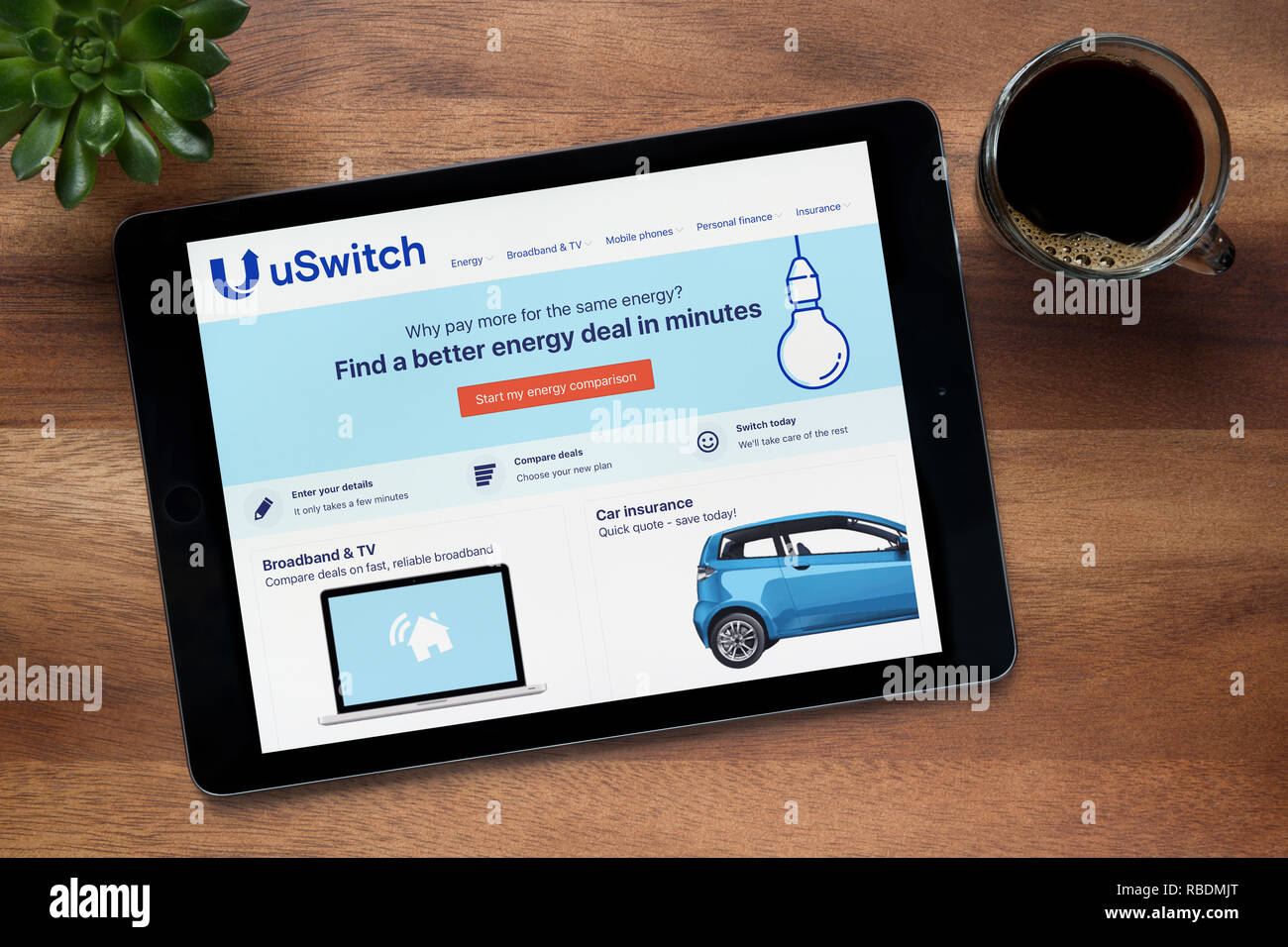 Il sito web di uSwitch è visto su un tablet iPad, su di un tavolo di legno lungo con un caffè espresso e una pianta di casa (solo uso editoriale). Foto Stock