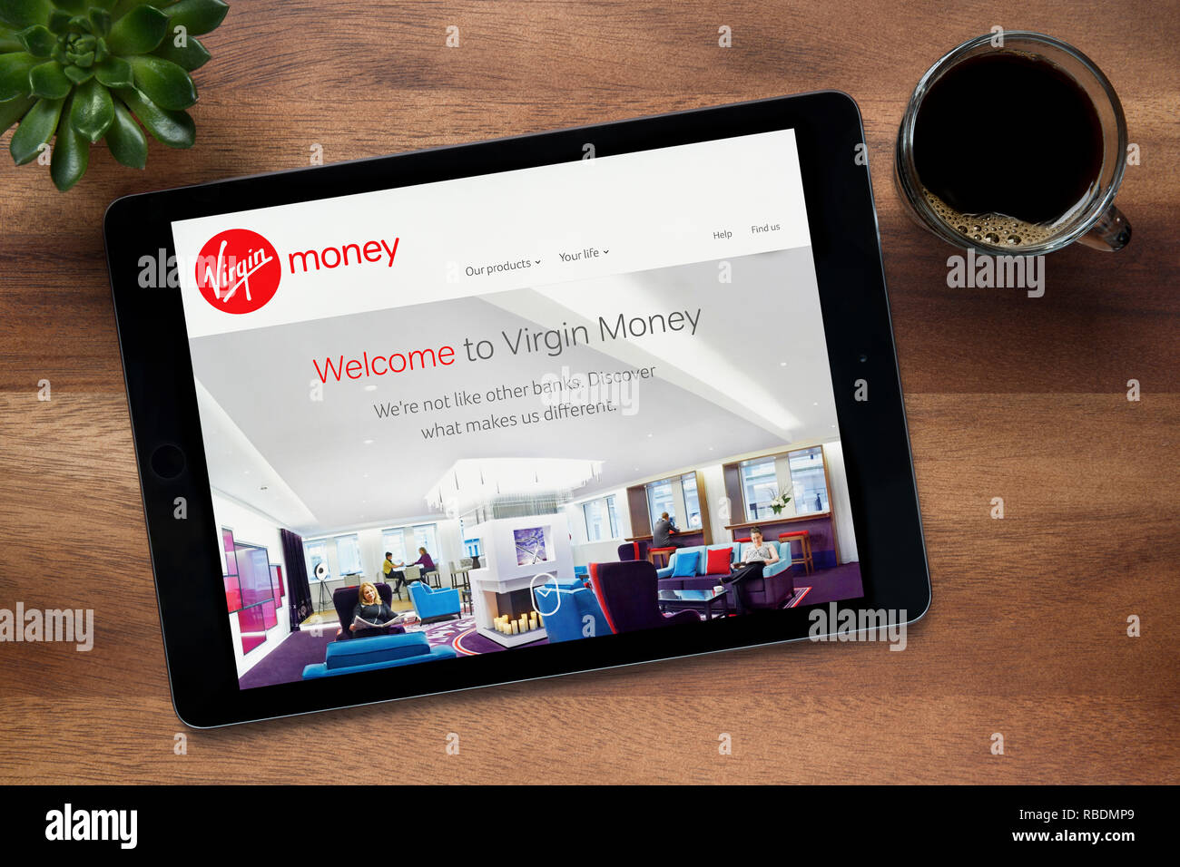 Il sito web della Vergine il denaro è visto su un tablet iPad, su di un tavolo di legno lungo con un caffè espresso e una pianta di casa (solo uso editoriale). Foto Stock