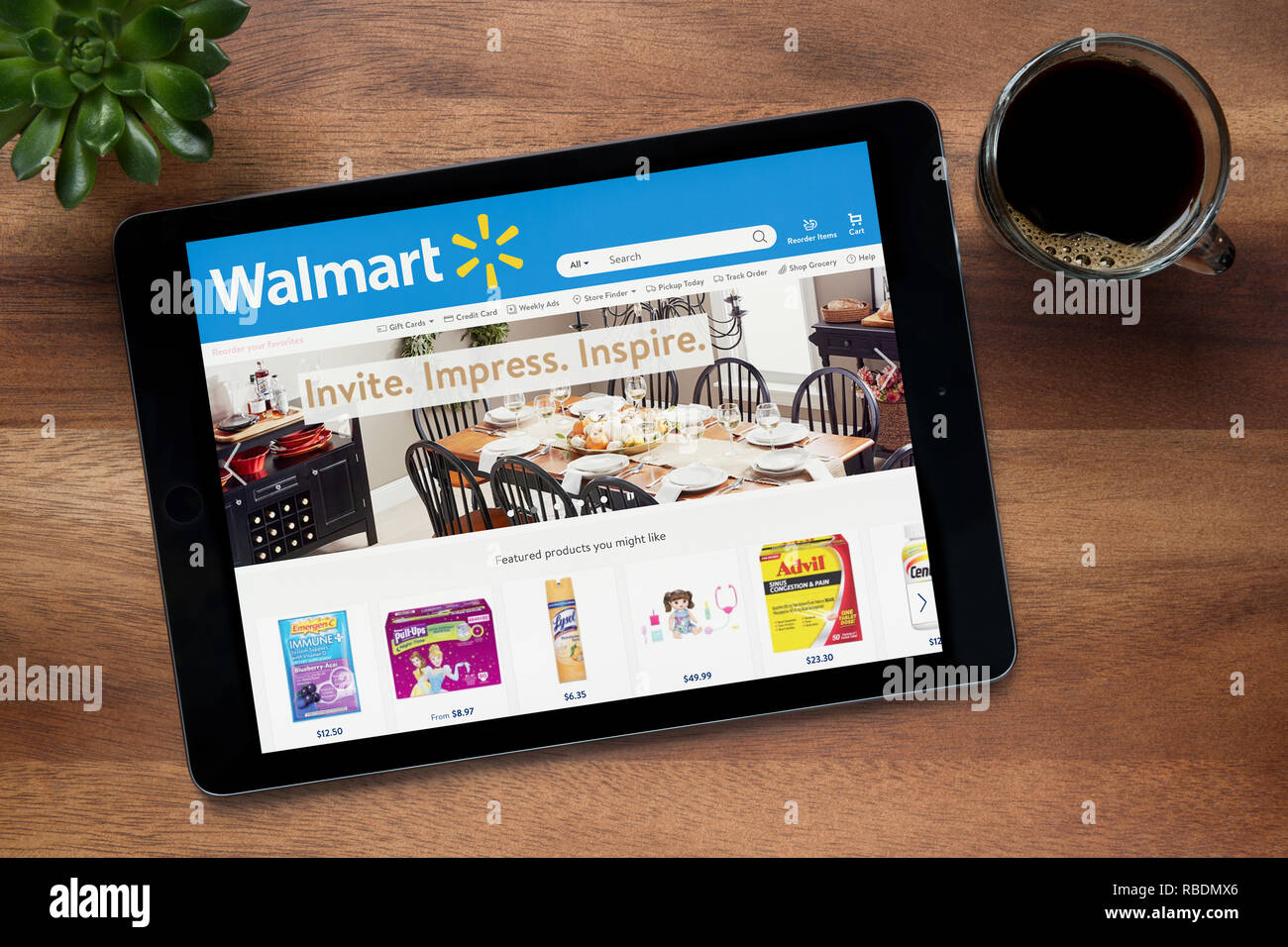 Il sito web di Walmart è visto su un tablet iPad, su di un tavolo di legno lungo con un caffè espresso e una pianta di casa (solo uso editoriale). Foto Stock