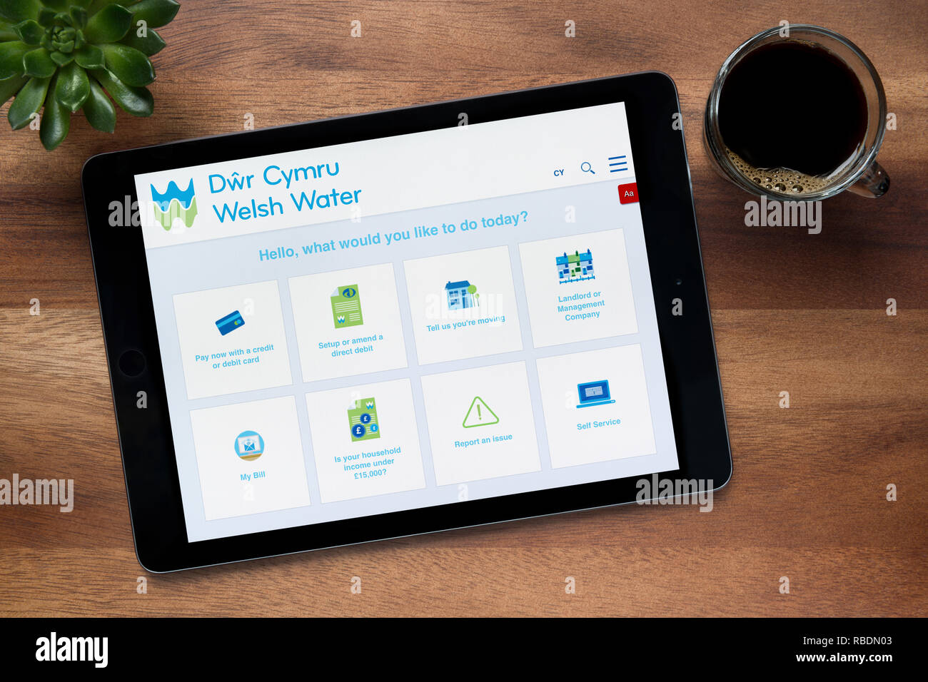 Il sito web di Welsh acqua è visto su un tablet iPad, su di un tavolo di legno lungo con un caffè espresso e una pianta di casa (solo uso editoriale). Foto Stock