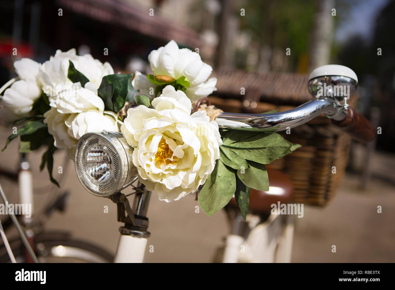 Close-up di stile retrò bicicletta con fiori artificiali (rose bianche) sul manubrio. Messa a fuoco selettiva. Foto Stock