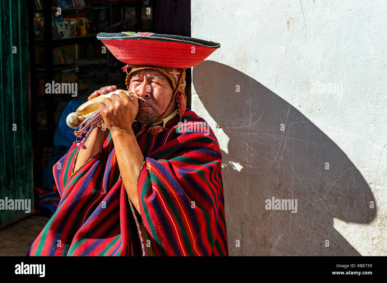 Ritratto di un peruviano Quechua horn soffiante con abbigliamento tradizionale, cappello e il poncho nel centro della città di Cusco, Perù. Foto Stock