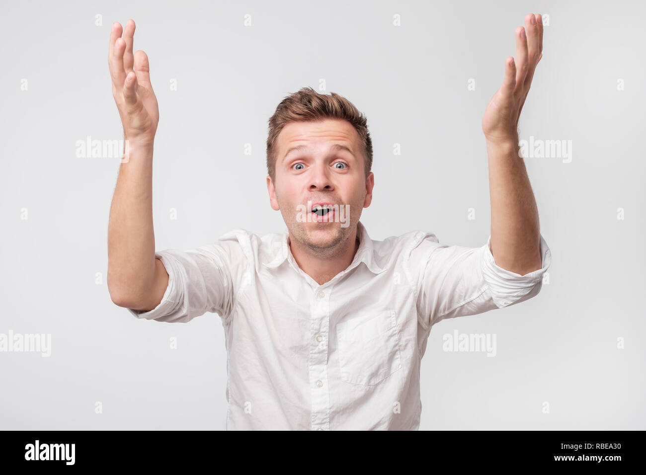 Felice l'uomo guarda con sorpresa e stupore di fronte, sollevando in alto le mani. Foto Stock