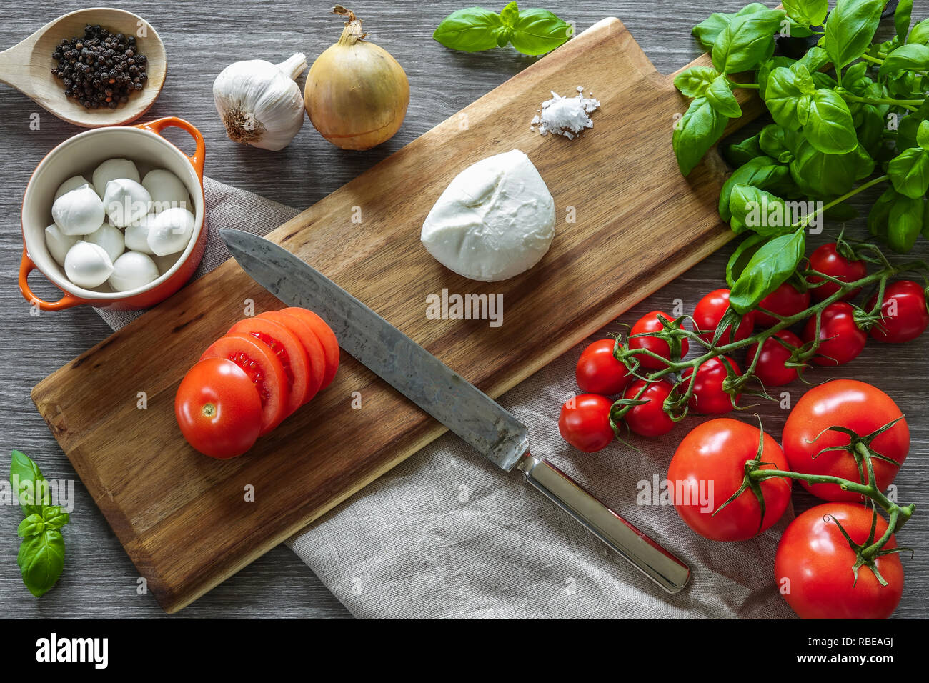 Il cibo italiano. Tagliere di legno circondato da cottura ingredienti, verdure e formaggio mozzarella su sfondo grigio. Foto Stock