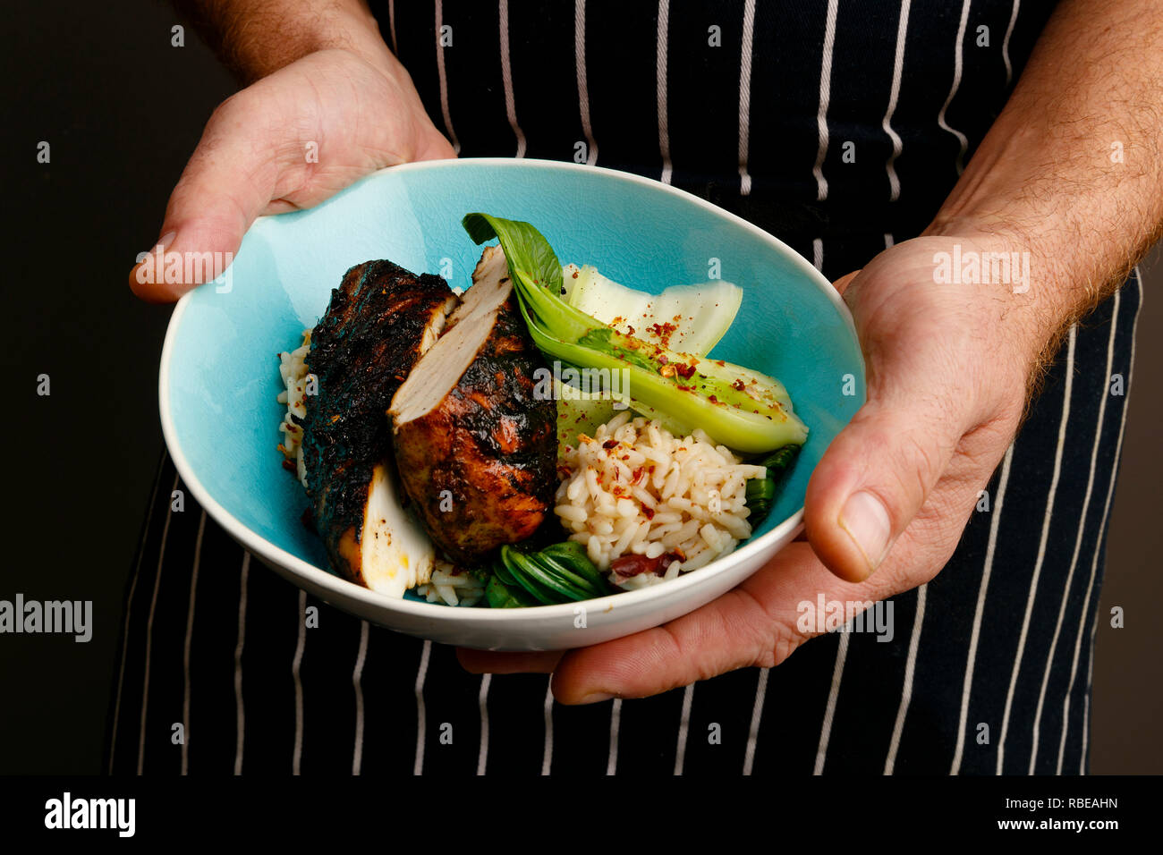 Close up di un chef mani presentando una ciotola di jerk pollo con riso e spezie e verdure Foto Stock