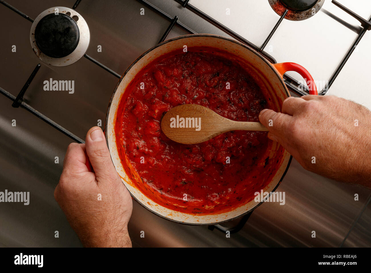 Vista in pianta di una pentola di gormet tradizionale salsa di pomodoro e il cucchiaio di legno su un acciaio inossidabile piano cottura Foto Stock