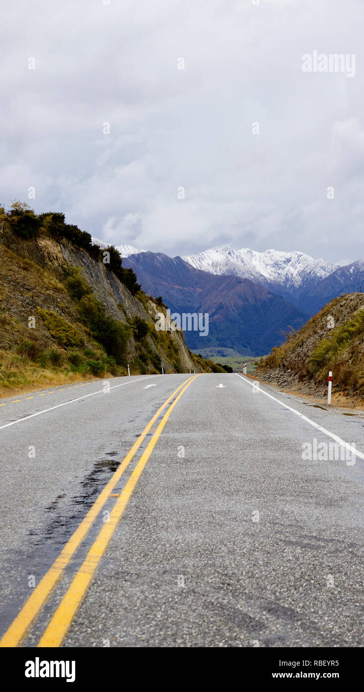 Autostrada vuoto scende nella valle, wiith montagne che sorgono su verde fondovalle Foto Stock