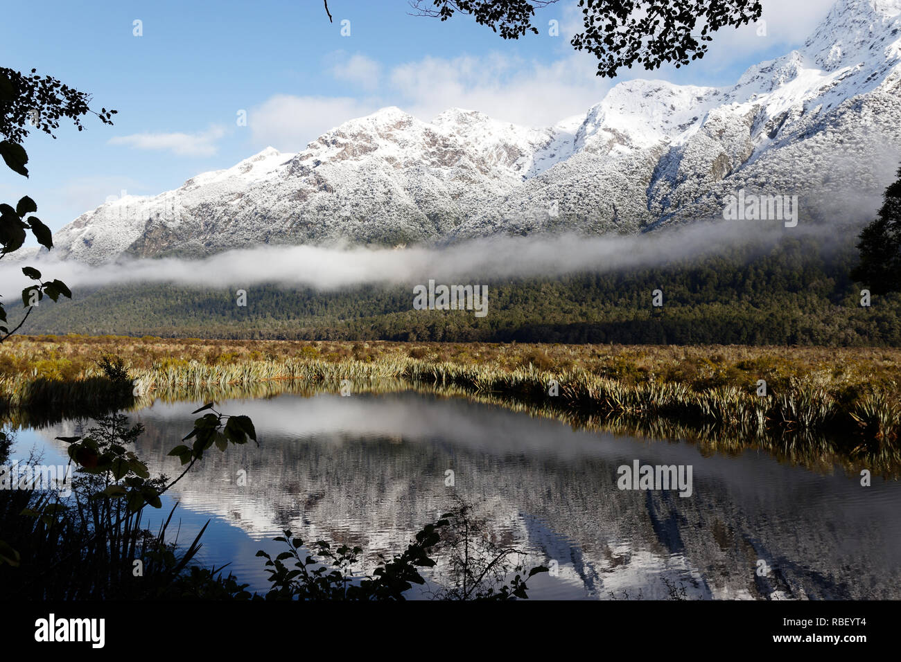 Nuova Zelanda Fiordlad montagne innevate riflette in stagno con nuvole basse intorno alla base Foto Stock