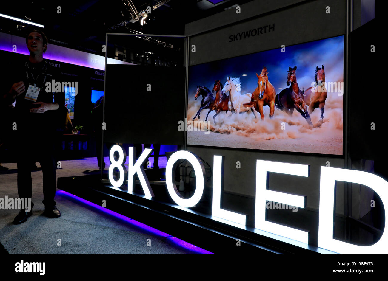 Las Vegas, Stati Uniti d'America. Il 9 gennaio, 2019. Un espositore sorge accanto a un 8K schermo OLED presso lo stand di Skyworth durante il Consumer Electronics Show (CES) di Las Vegas, Stati Uniti, gennaio 9, 2019. Come il CES annuale ha dato dei calci a fuori qui Martedì, mondo tech le aziende stanno cogliendo le opportunità di rafforzare la cooperazione con le imprese cinesi, occhiatura il mercato cinese, tecnologia e talento. Credito: Li Ying/Xinhua/Alamy Live News Foto Stock