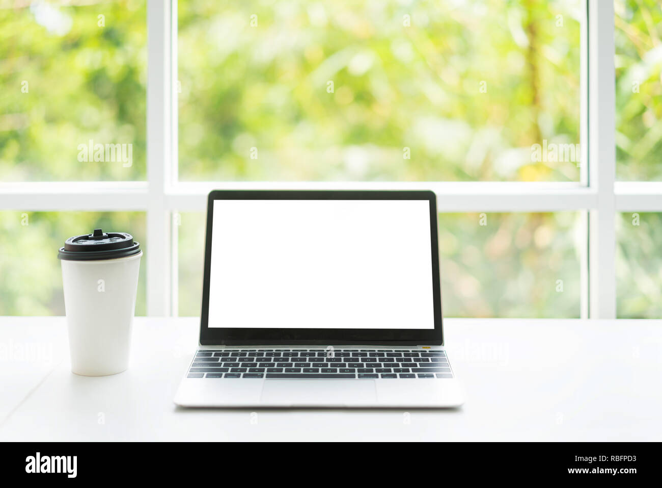 Lo schermo è vuoto il computer portatile e la tazza di caffè sul tavolo al caffè cafe con la natura in background. Tecnologia e business moderno concetto di vita Foto Stock