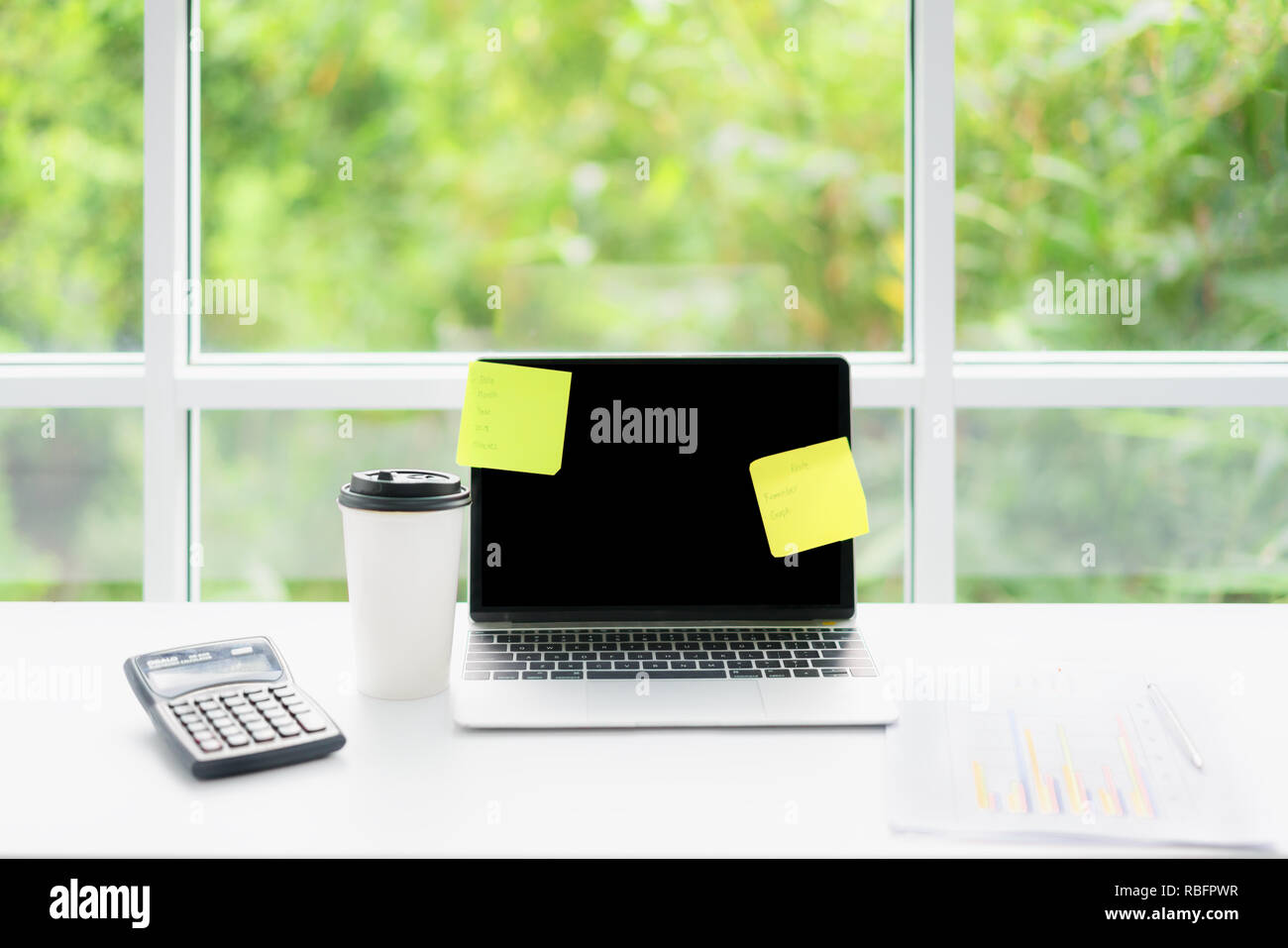 Lo schermo è vuoto il computer portatile e la tazza di caffè sul tavolo al caffè cafe con la natura in background. Tecnologia e business moderno concetto di vita Foto Stock