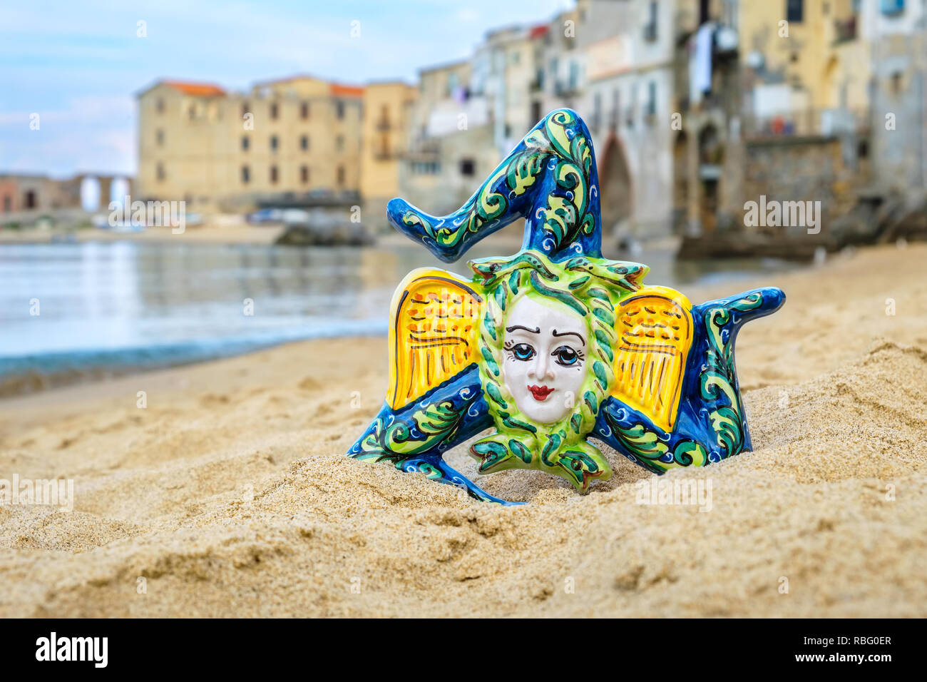 Tradizionale souvenir siciliano - Trinacria in ceramica su una spiaggia di sabbia a Cefalu. Sicilia, Italia Foto Stock