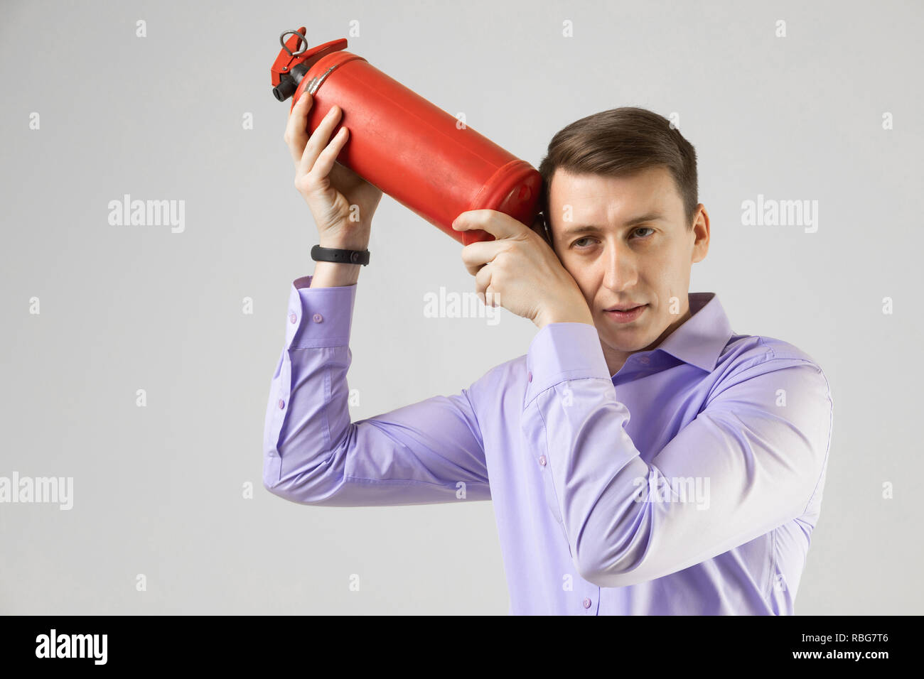 Giovane uomo messo un estintore per la sua testa isolata su sfondo chiaro Foto Stock