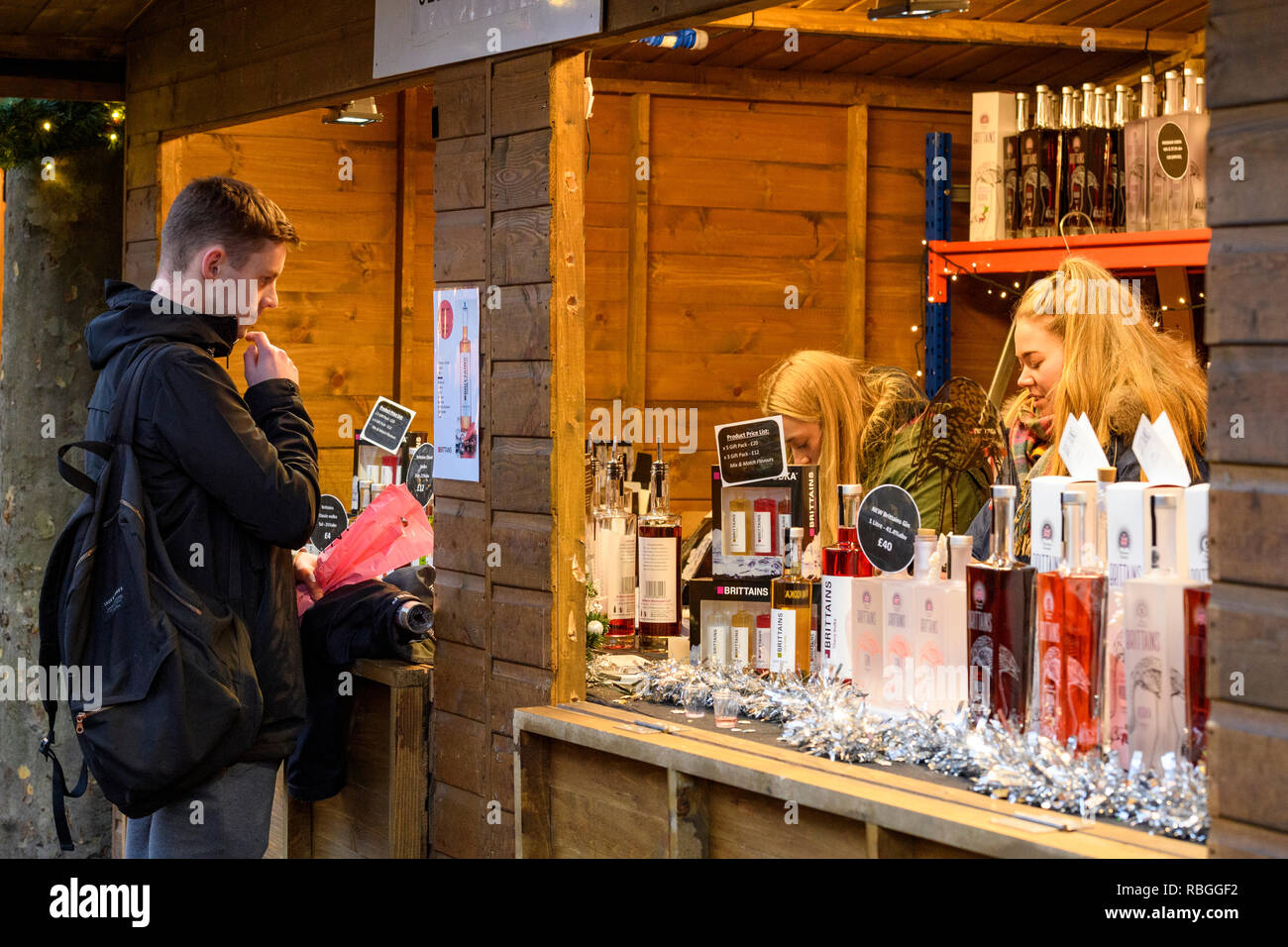 Le persone che lavorano nella bancarella vendendo Brittain il gin e la vodka e il potenziale cliente al Mercato di Natale guardando il listino prezzi sul display - York, Inghilterra, Regno Unito. Foto Stock