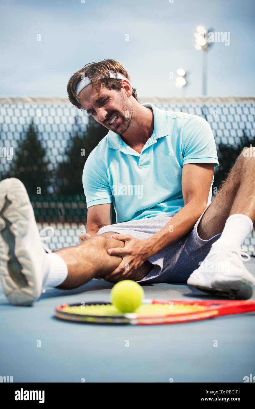 Lesioni sportive. Giovane giocatore di tennis di toccare il suo ginocchio mentre è seduto sul campo da tennis Foto Stock