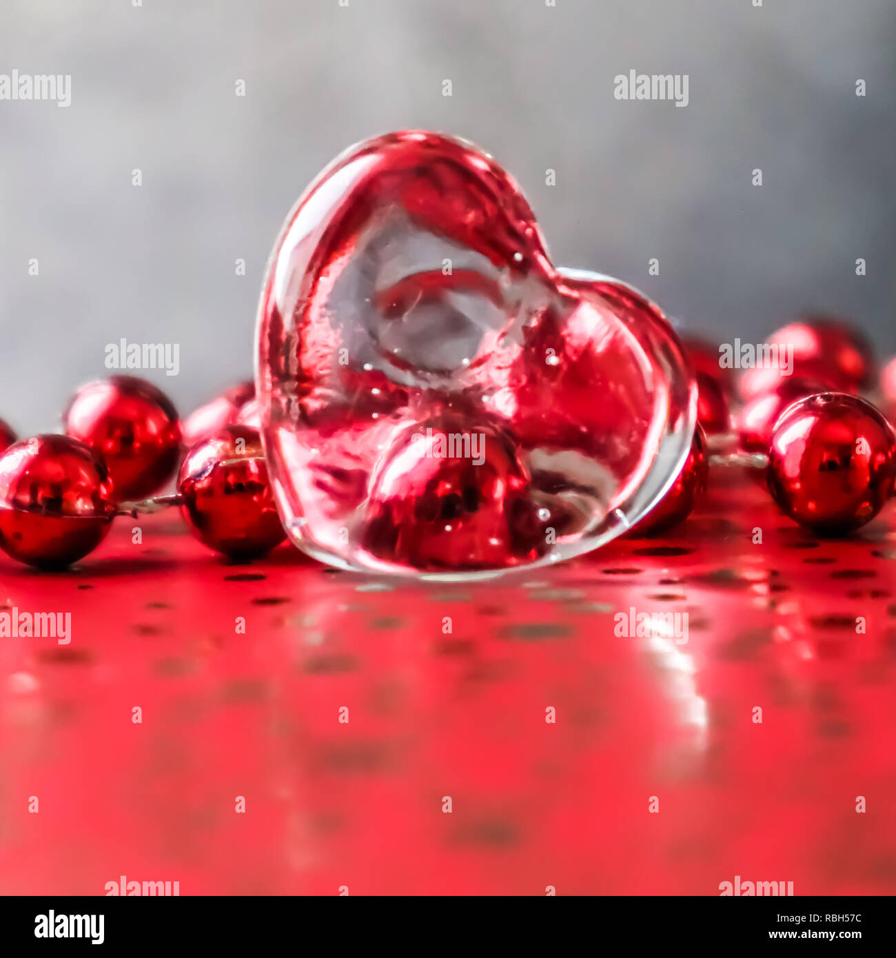 Fulgido cuore trasparente e un gruppo di perle di rosso. San Valentino perfetto biglietto di auguri sfondo. Immagine in tono di colore rosso su sfondo grigio in un 1x1 Foto Stock