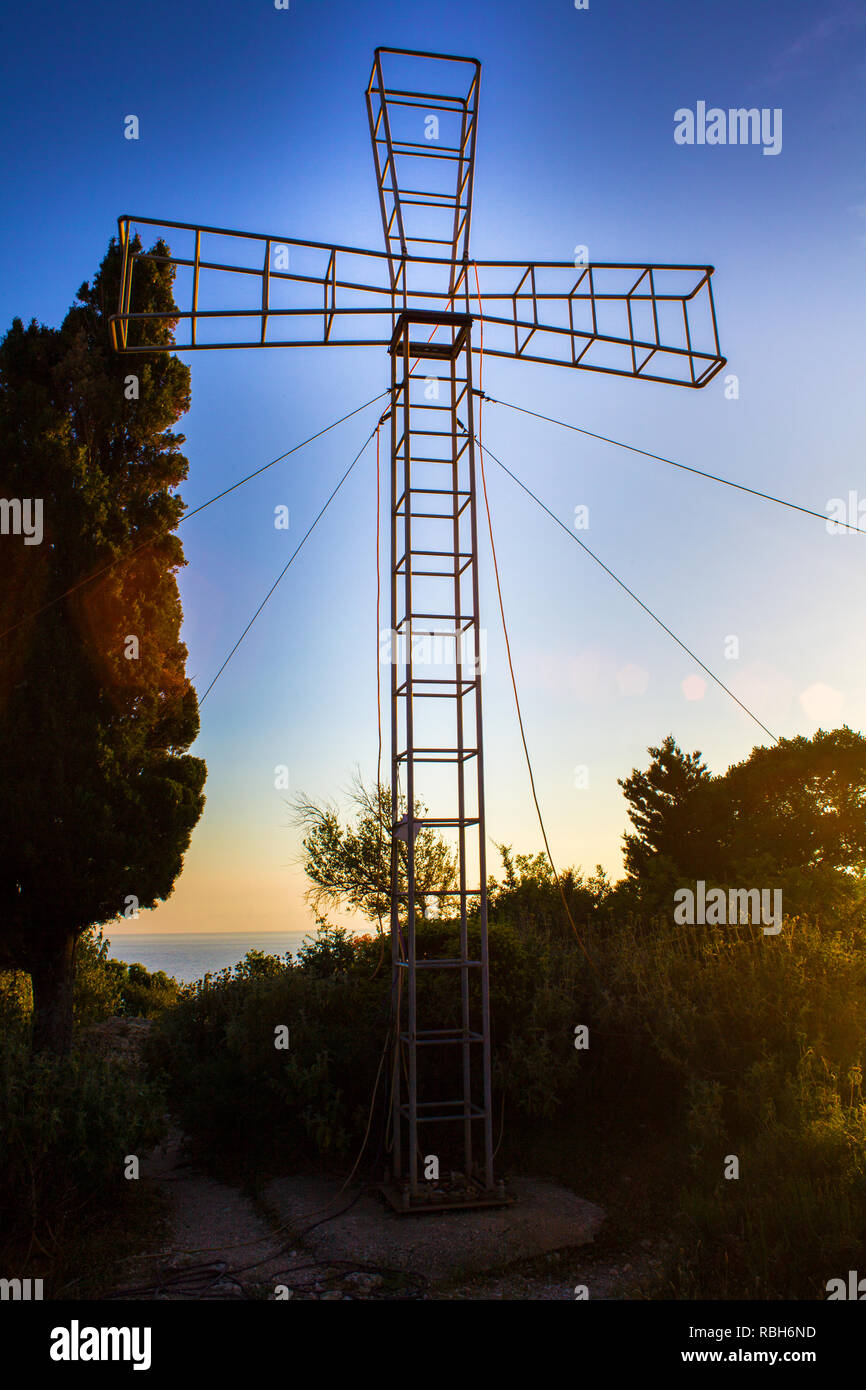 Torre Steelframe in piedi la forma di una croce. Struttura verticale supportato da Guy filo del cavo. Piante circondano icona religiosa permanente sulla cementata Foto Stock
