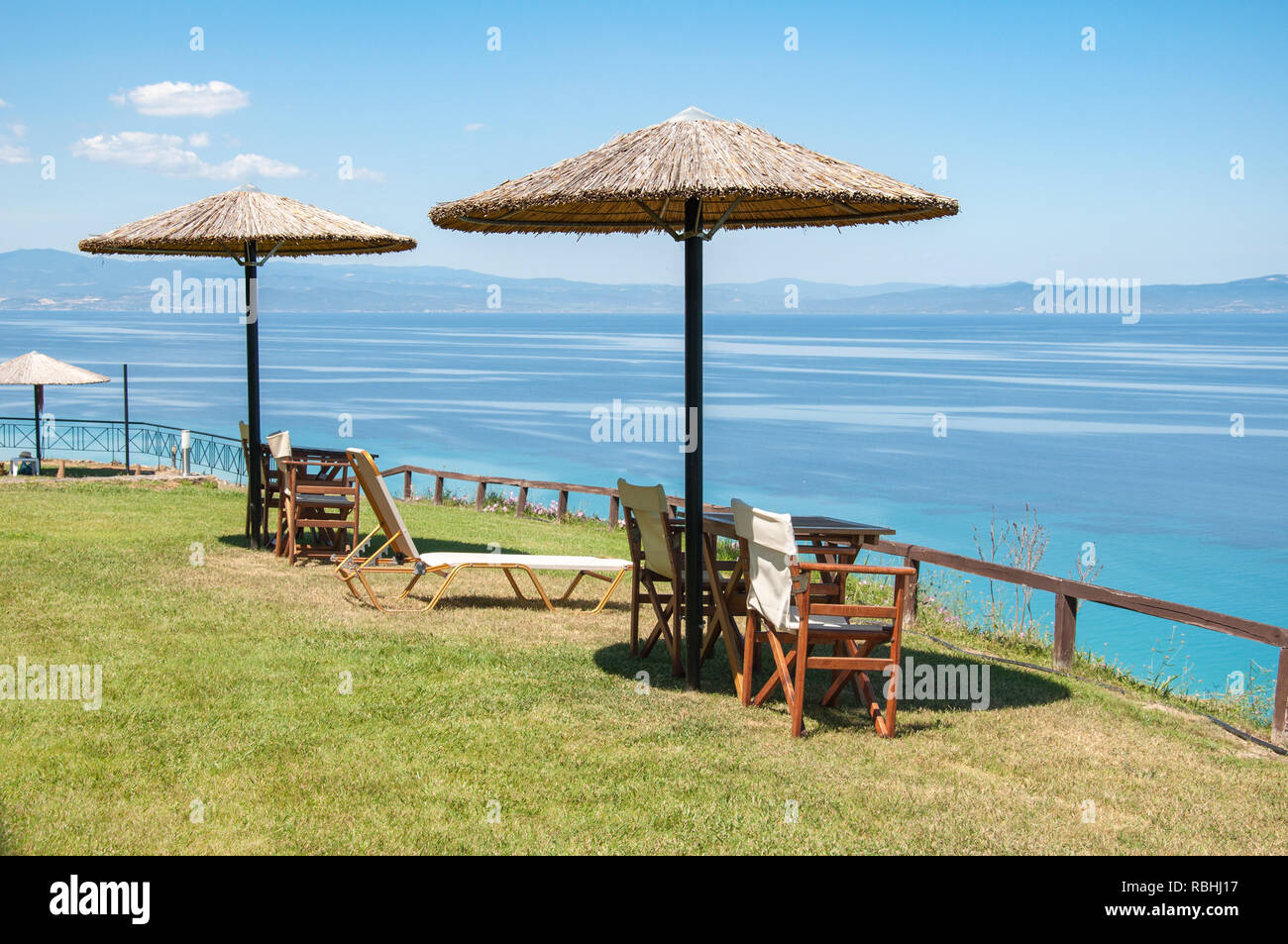 Ombrelloni di paglia forniscono ombra per tavoli e sedie che si affaccia sul Golfo Kassandras in Halkidiki, Grecia Foto Stock
