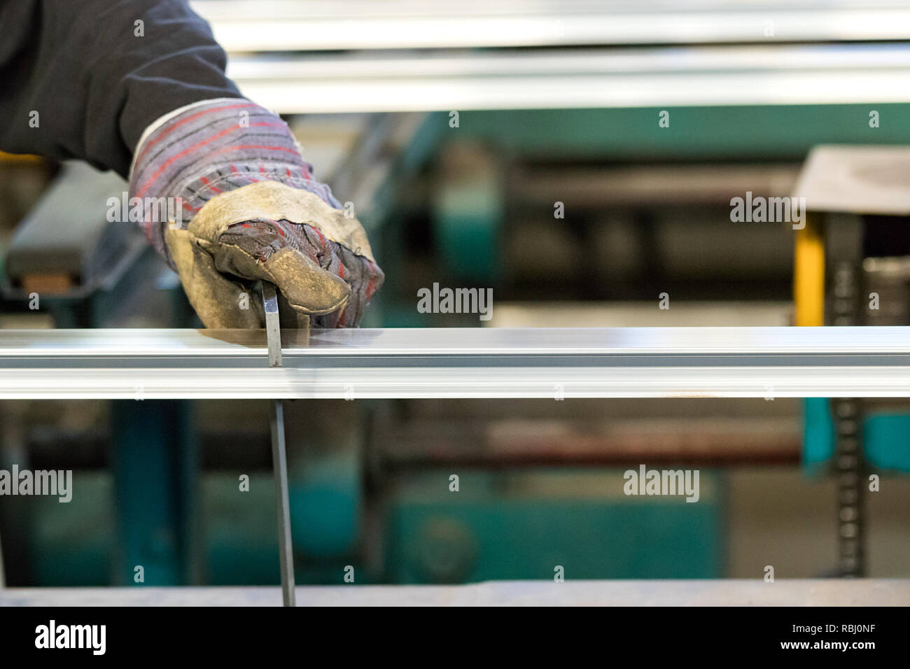 Un uomo operatore della macchina utilizzando i guanti di sicurezza il controllo del tratto di un profilo in alluminio con una squadra. Foto Stock