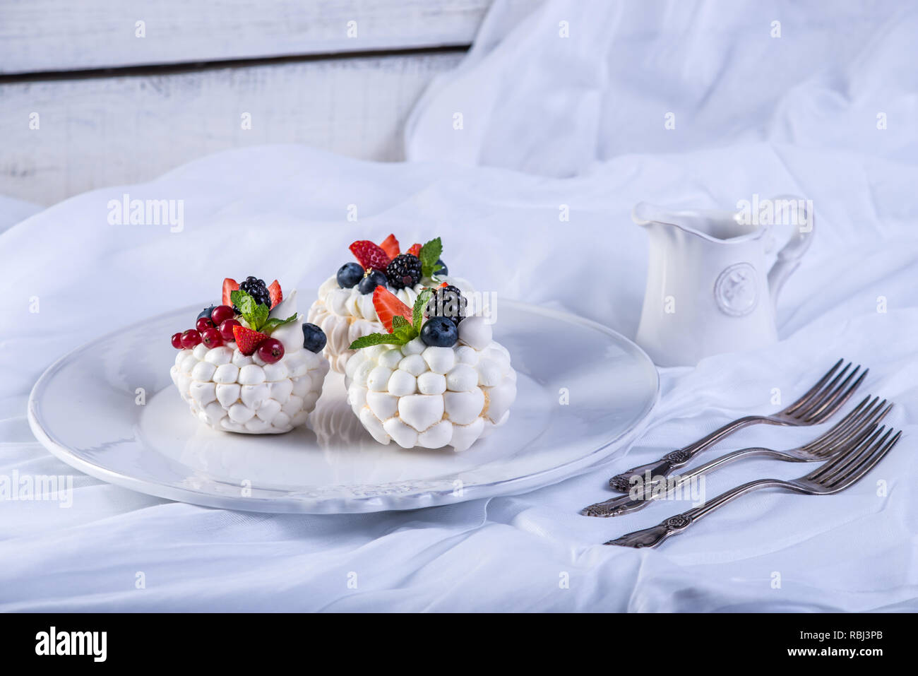 Bianco delicato meringhe con frutti di bosco freschi sulla piastra. Il dessert Pavlova. Sfondo bianco. Una festosa torta nuziale. Foto Stock