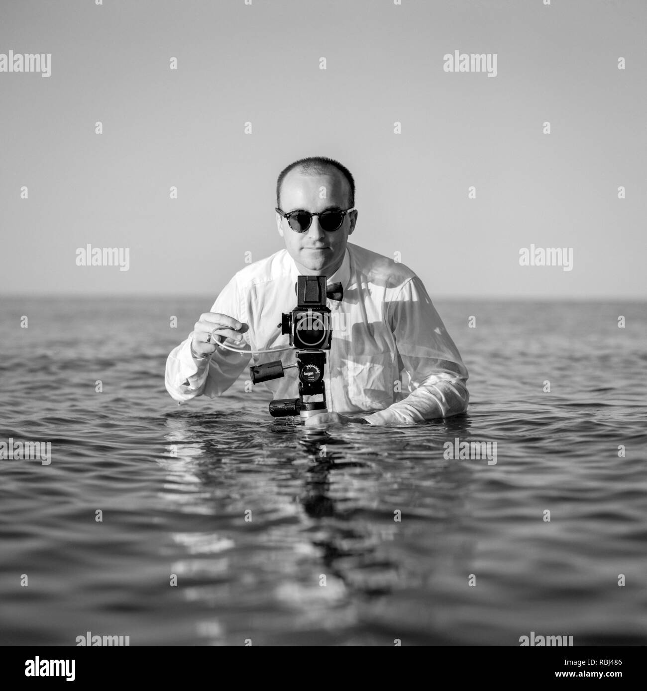 Giovane fotografo in piedi in acqua e tenendo fotocamera di medio formato. Spiaggia di Southampton, New York, USA 40-45 anni, 45-50 anni, 50-59 anni, Foto Stock