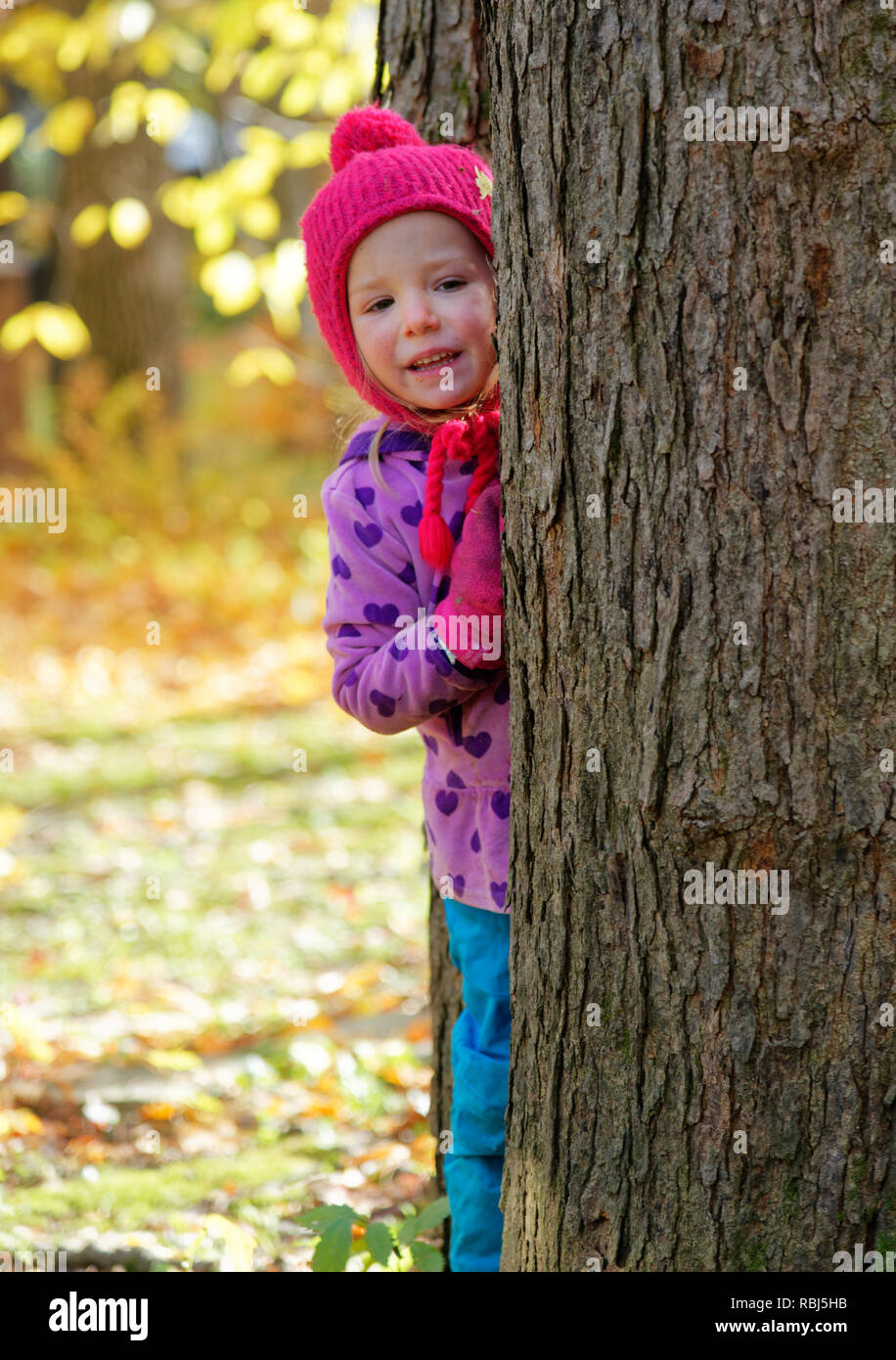 Una bambina di 4 anni) guardando fuori dal tra due alberi Foto Stock