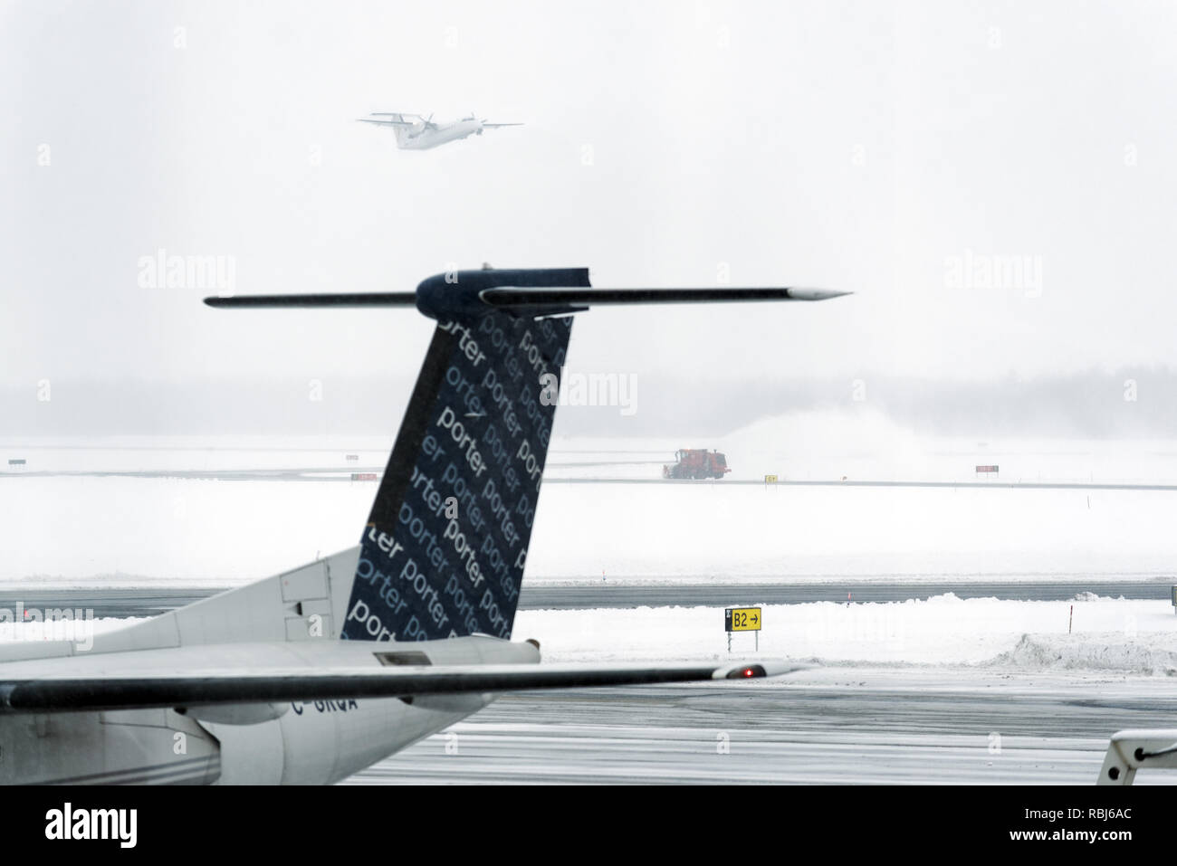 Un piano tenendo fuori nella nebbia mentre uno spartineve cancella la pista - condizioni invernali a Quebec City Jean Lesage airport Foto Stock