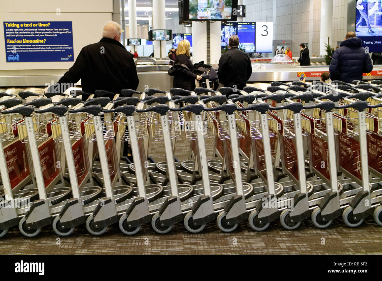 Persone in piedi da filari di carrelli portabagagli in Toronto Pearson airport in attesa per i loro bagagli per arrivare. Foto Stock