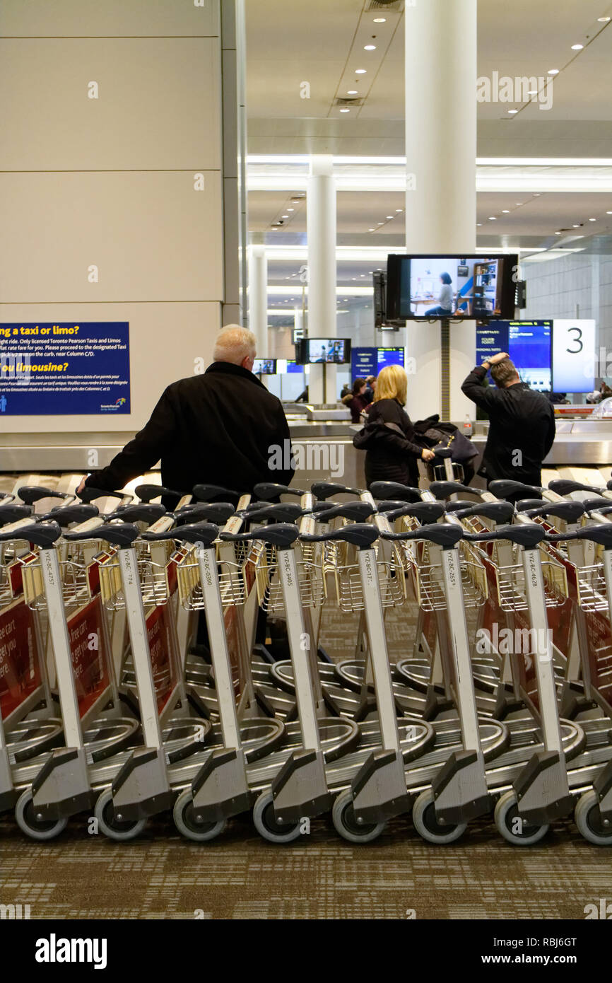 Persone in piedi da filari di carrelli portabagagli in Toronto Pearson airport in attesa per i loro bagagli per arrivare. Foto Stock
