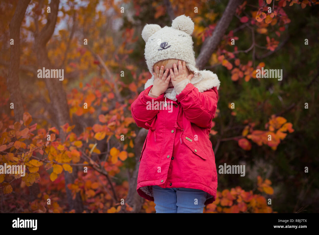 Carino giovane ragazza russa elegante vestito di rosso Caldo giubbotto fatti a mano jeans blu stivali e agganciato hat orsacchiotto che pongono in autunno colorato pathwa foresta Foto Stock