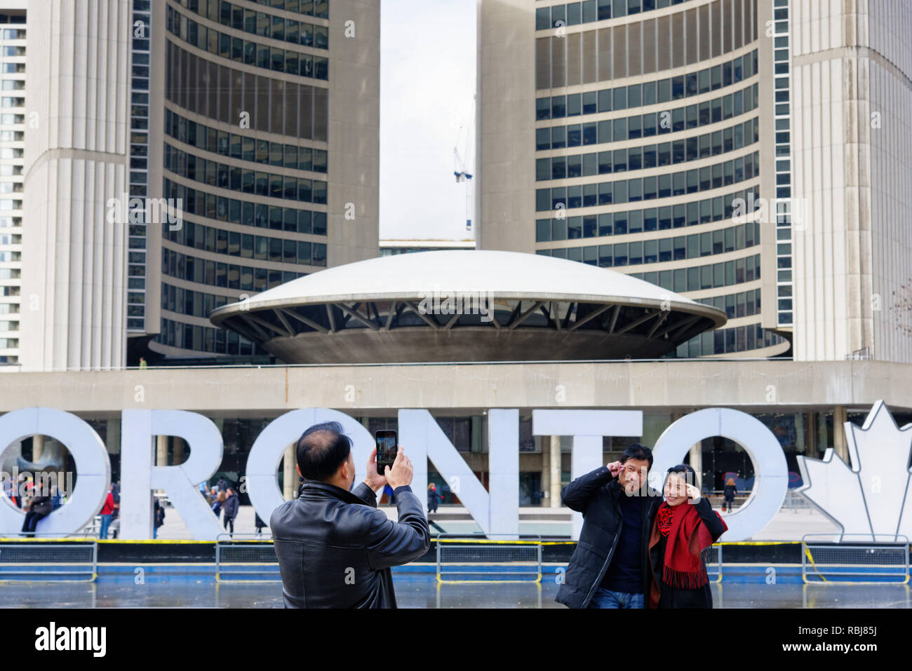 Una coppia asiatica che posano per una foto di loro di fronte al segno di Toronto su Nathan Phillips Square, Toronto, Canada Foto Stock