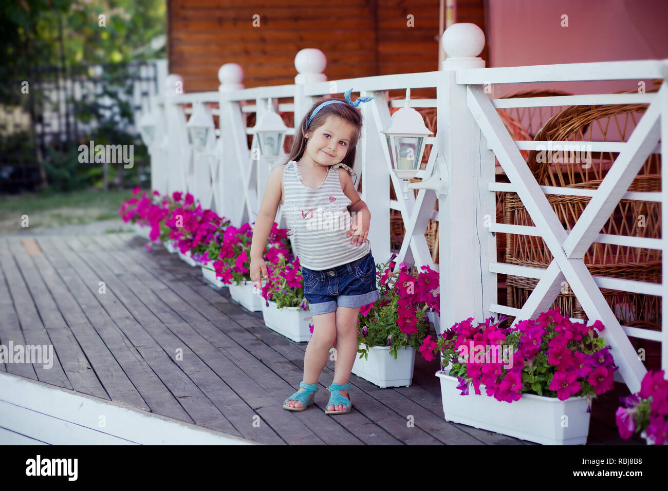 Bellissima ed elegante simpatico baby girl Brunette con capelli in posa su legno giardino pieno di fiori che indossa jeans minuscole magliette e ariosa skivy underwaist e b Foto Stock